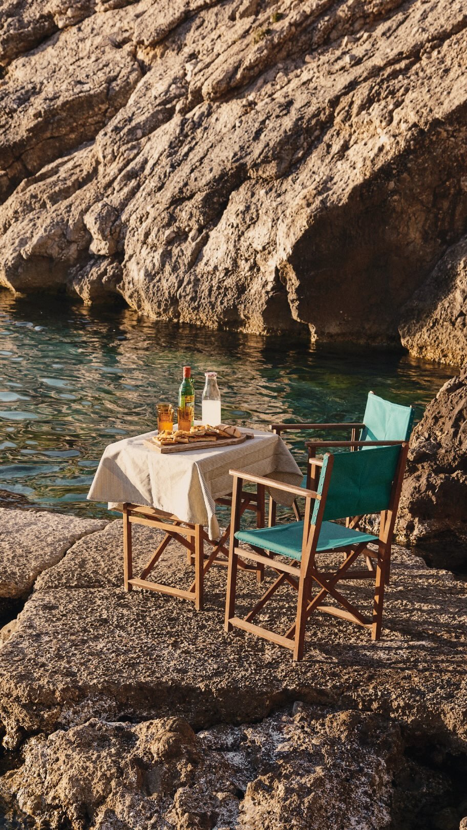 Mesa junto al agua con dos sillas y bebidas.