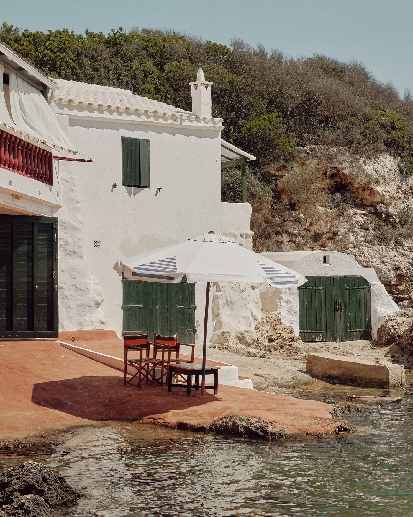 Casa blanca junto al mar con dos sillas y una sombrilla